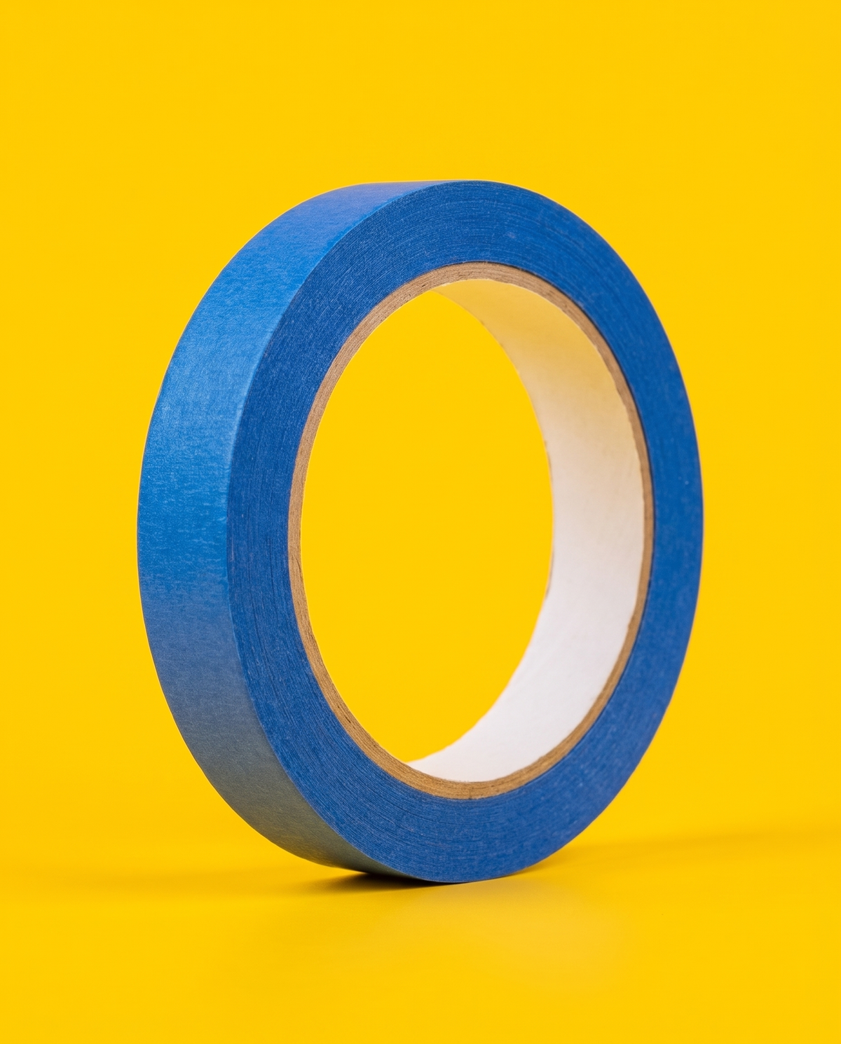Roll of blue masking tape, 1 inch wide, standing on edge on a yellow background